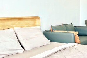 Un lit avec une tête de lit en bois, un canapé vert et un oreiller blanc.