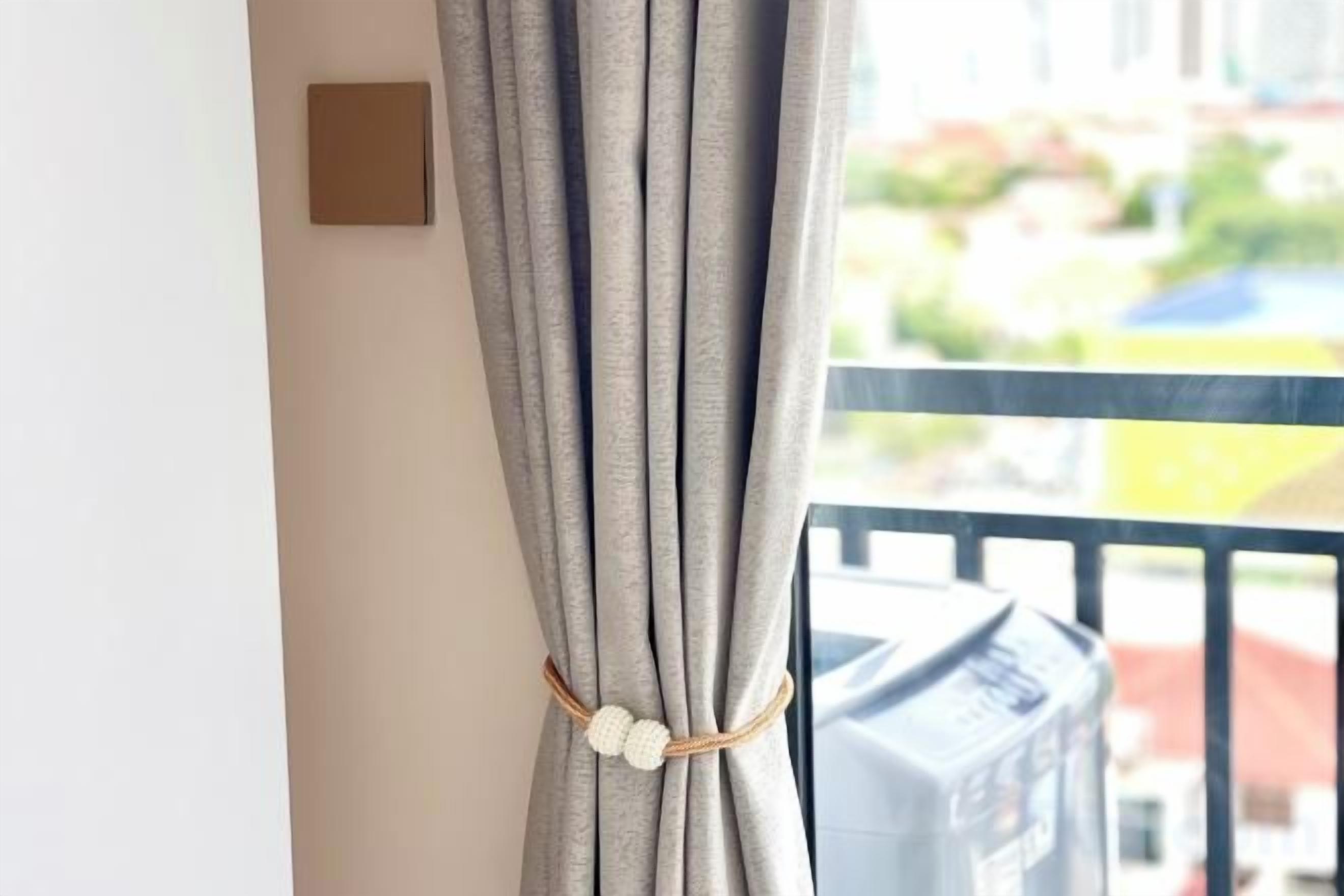 Une fenêtre avec un rideau retenu par un cordon, dévoilant un balcon doté d’une balustrade.