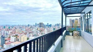 A balcony with a city view, a glass railing, and a small table with chairs.