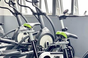 Reihe von stehenden Fahrrädern in einem Fitnessstudio mit einem Fenster im Hintergrund.