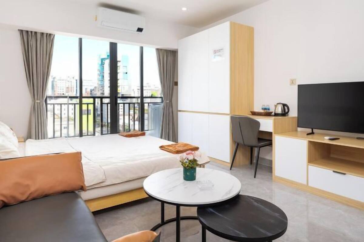 Una habitación de hotel moderna con cama, una mesa redonda, televisor y balcón con vista a la ciudad.