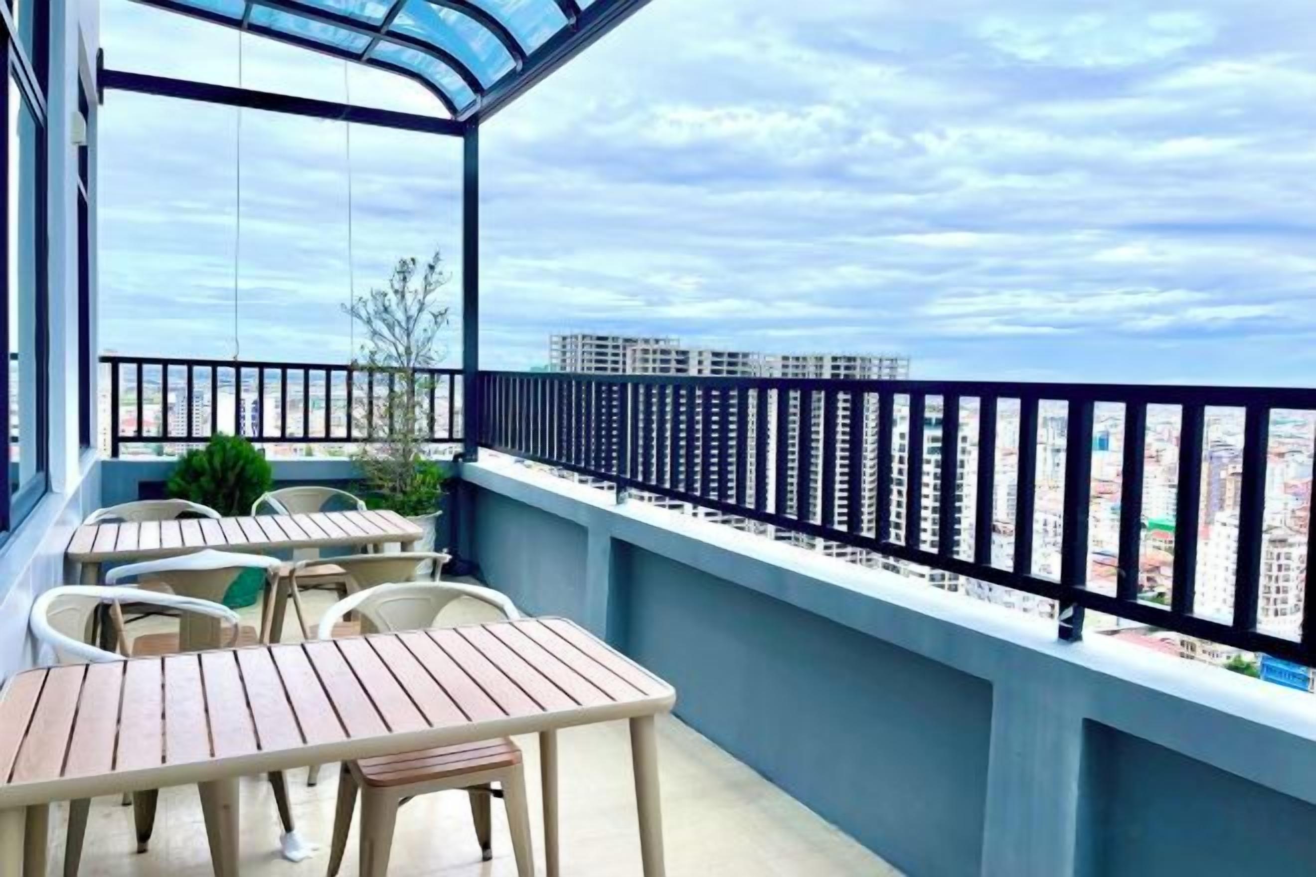 A balcony with tables and chairs, a glass enclosure, and a city view.