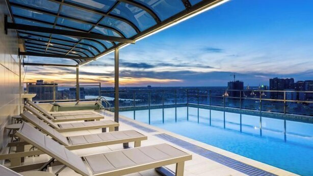 A rooftop infinity pool with lounge chairs and a glass canopy.