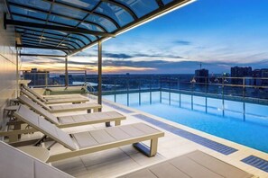 Une piscine à débordement située sur le toit, avec des chaises longues et une verrière.