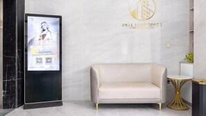 A modern lobby with a marble wall, a digital display, a sofa, and a gold-framed table.