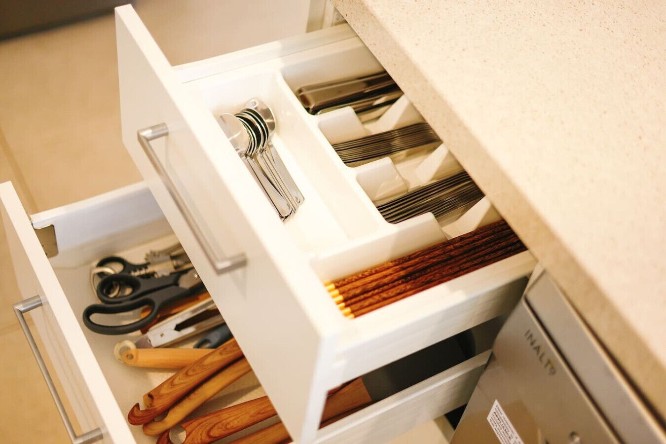 A drawer with various kitchen utensils, including scissors, a whisk, and wooden spoons.
