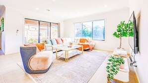 A spacious living room with a sofa set, a coffee table, and a television. - StayAU 4BR Tranquil Family Escape House Point Cook (Point Cook)