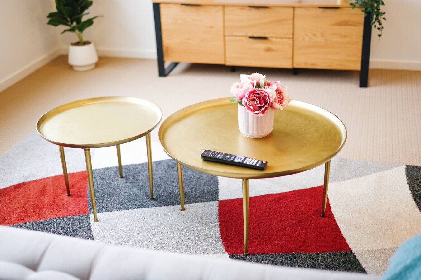 Deux tables rondes aux pieds dorés, une télécommande posée sur l’une, et un vase rempli de fleurs sur l’autre.