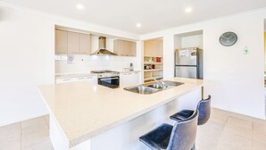 A modern kitchen with a central island, stainless steel appliances, and a clock on the wall. - StayAU 4BR Tranquil Family Escape House Point Cook (Point Cook)