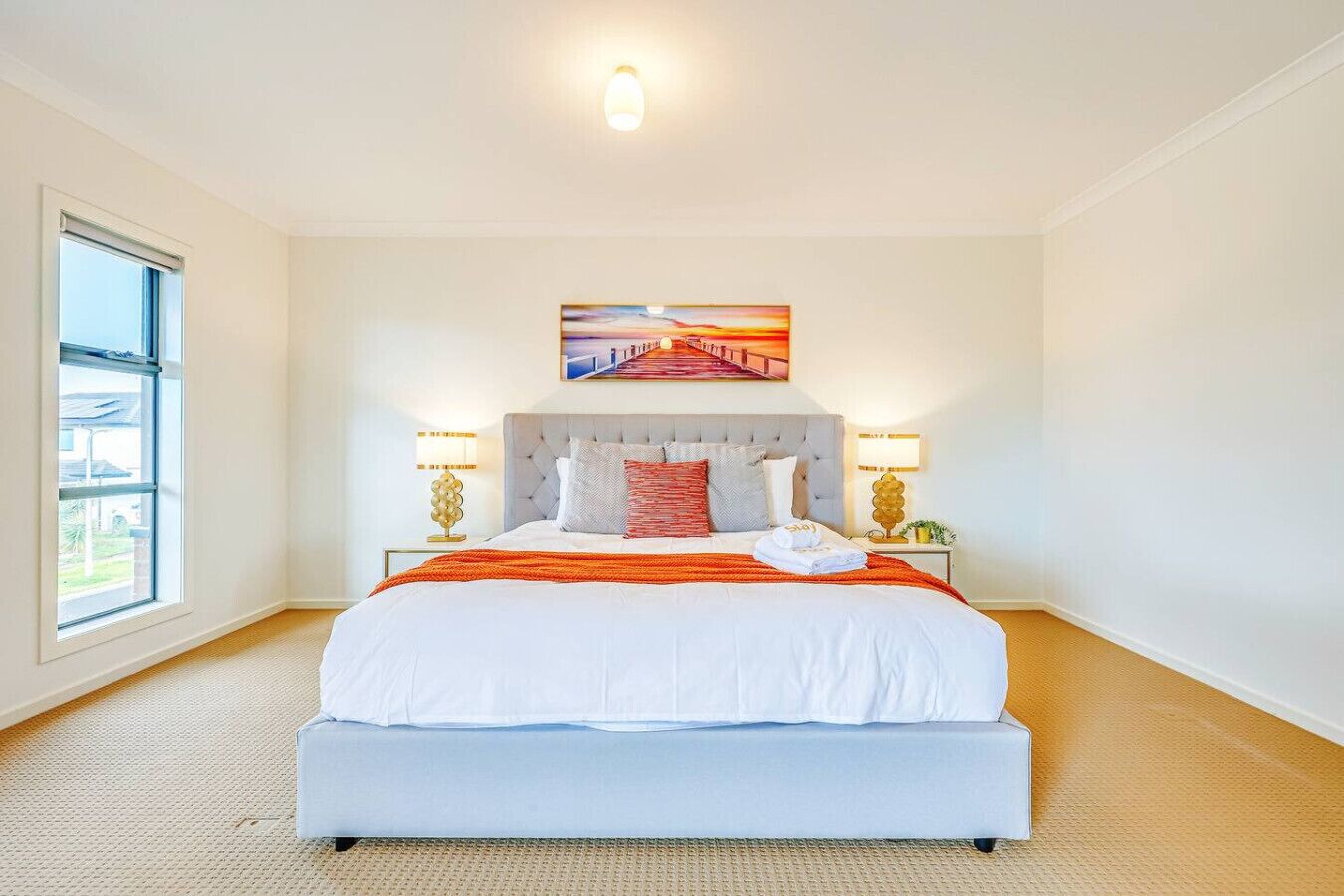 A spacious bedroom with a large bed, a view of a bridge through the window, and a painting above the bed.