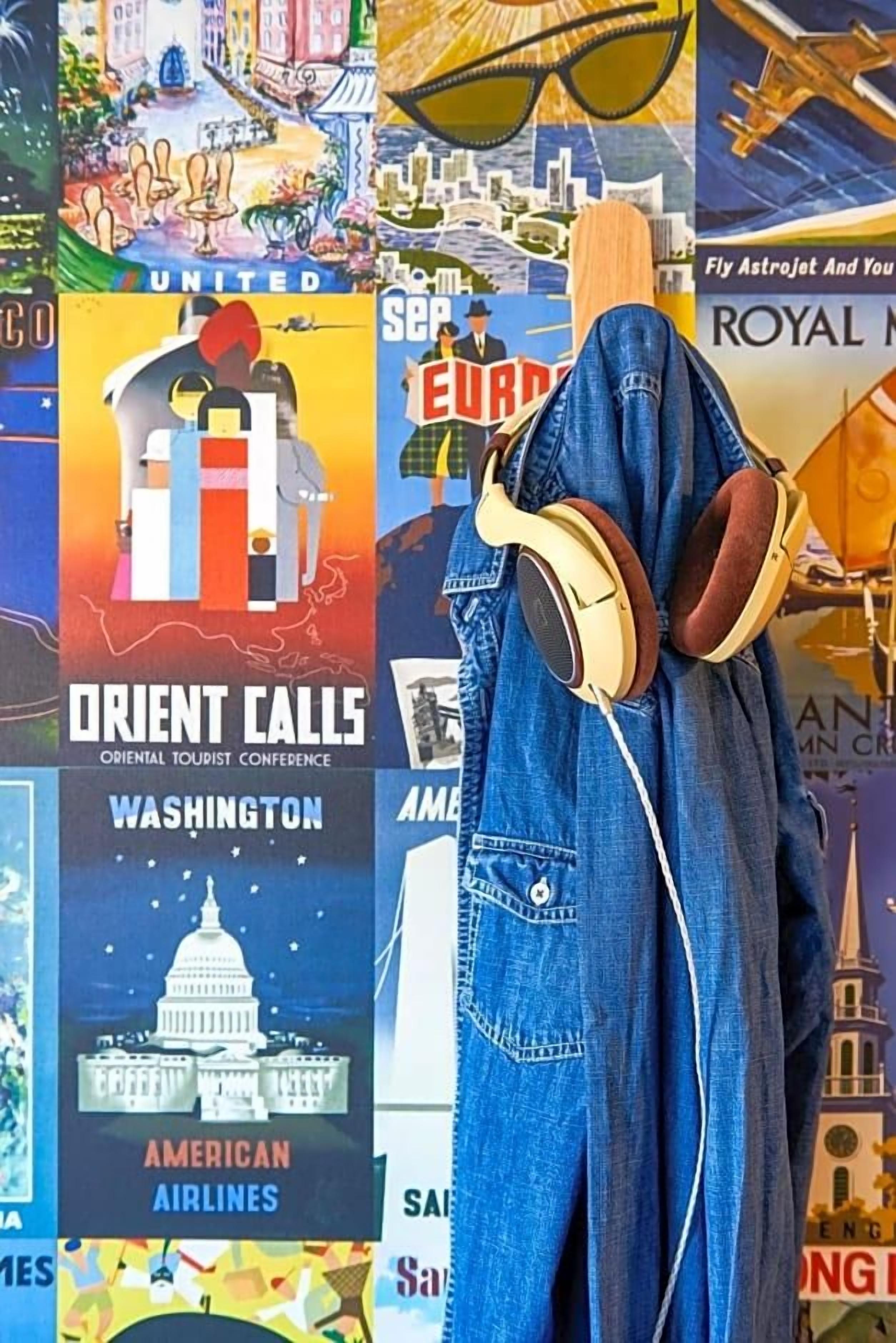 Una persona con cuffie e una giacca di jeans, in piedi di fronte a un muro con diversi manifesti di viaggio.