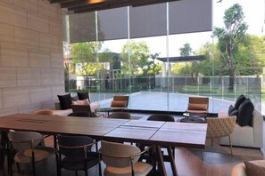 A modern dining area with a long table and chairs, large windows, and a view of the outdoors. - Andromeda Condominium Seaview Amazing Room (Pattaya)