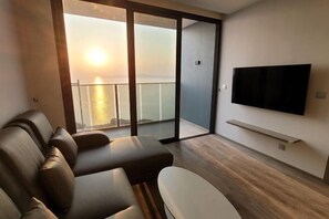 Una sala de estar moderna con un sofá, un televisor montado en la pared y un balcón con vista al mar.