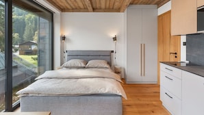 A modern bedroom with a wooden ceiling, a large bed, bedside lamps, and a view of the outdoors.