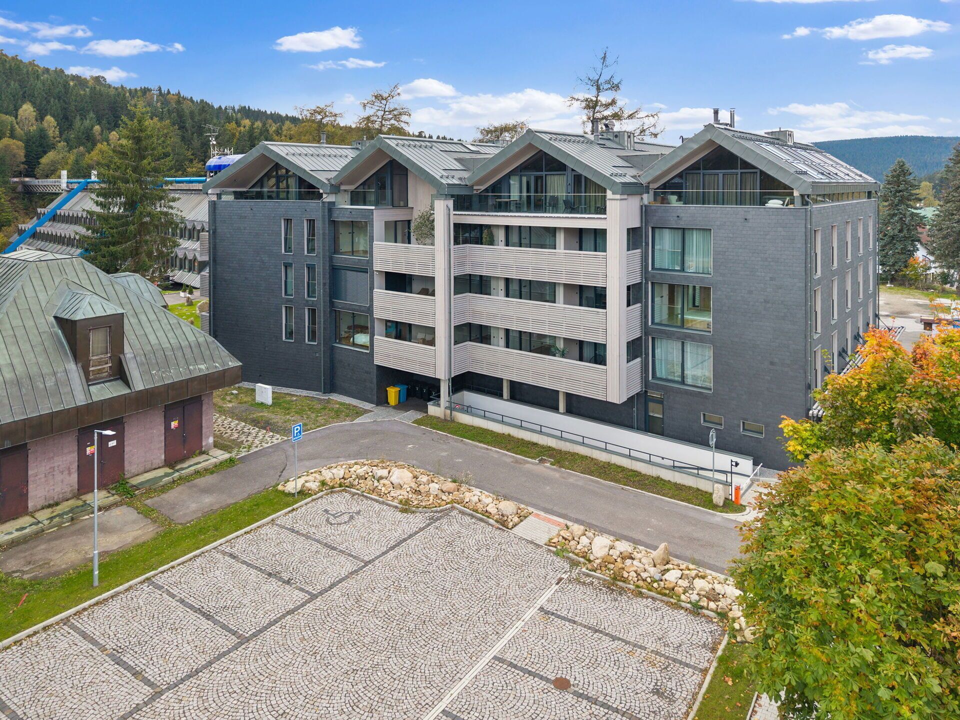 A modern multi-story building with a parking area and a small adjacent structure.