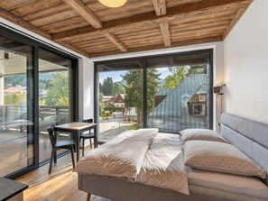 A modern bedroom with a large window, a wooden ceiling, and a view of a village.