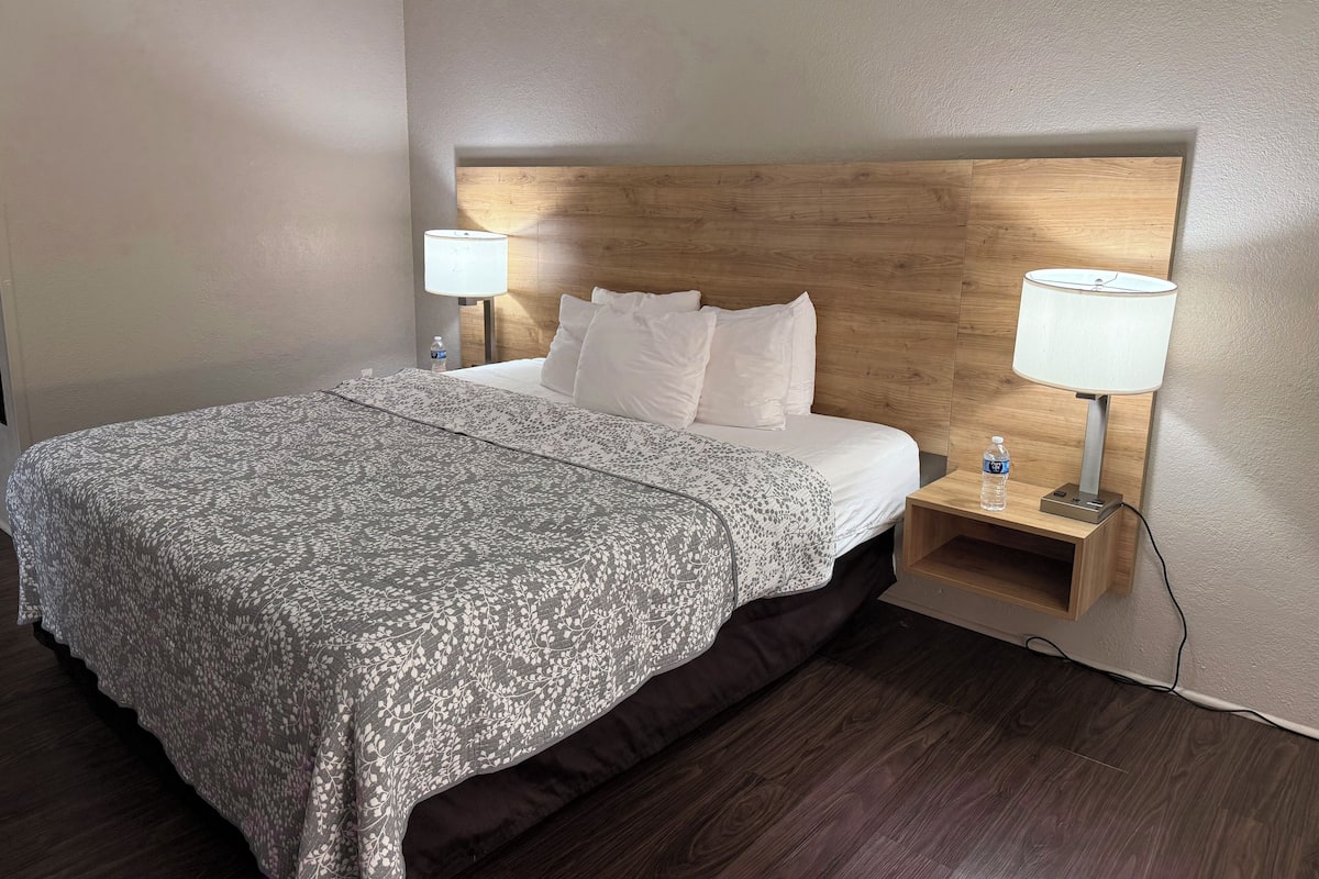 Une chambre d’hôtel avec un lit, deux lampes de chevet, une bouteille d’eau et une tête de lit en bois.