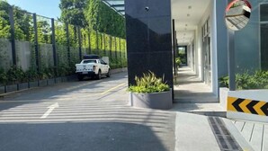 Μια σύγχρονη είσοδος κτιρίου με ένα λευκό αυτοκίνητο σταθμευμένο στο εσωτερικό, μια σκεπαστή στοά και μια κάμερα ασφαλείας.