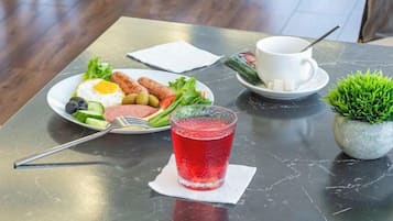 Una mesa con un plato de huevos, verduras y una bebida roja, acompañado de una taza y platillo blancos.