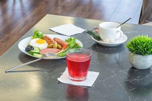 A table with a meal consisting of eggs, vegetables, and a red drink, accompanied by a white cup and saucer. - Oscar Hotel by AG Hotels Group (Almaty)