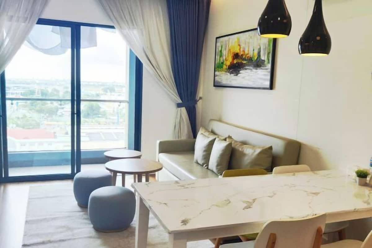 Un salon moderne avec un canapé, des tables rondes, une table à manger et une grande fenêtre avec des rideaux.
