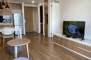 A modern kitchen with a refrigerator, a dining area with a table and chairs, and a television mounted on a wooden cabinet. - Republic Plaza -Luxury condo with pool, close to airport (Ho Chi Minh City)