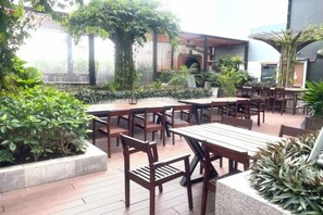 Un área de patio al aire libre con mesas y sillas de madera, rodeada de plantas en macetas y follaje.