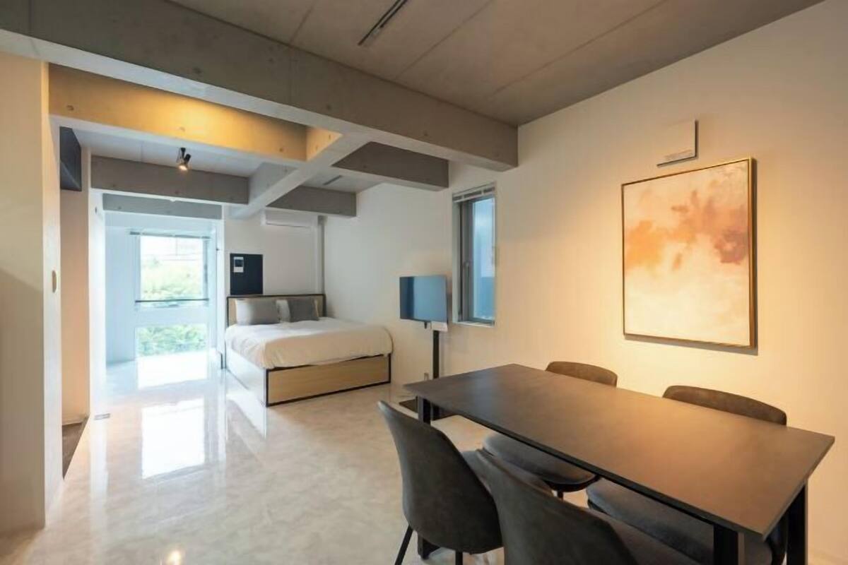 A modern hotel room with a bed, a desk, and a chair. There is a window with a view of greenery.
