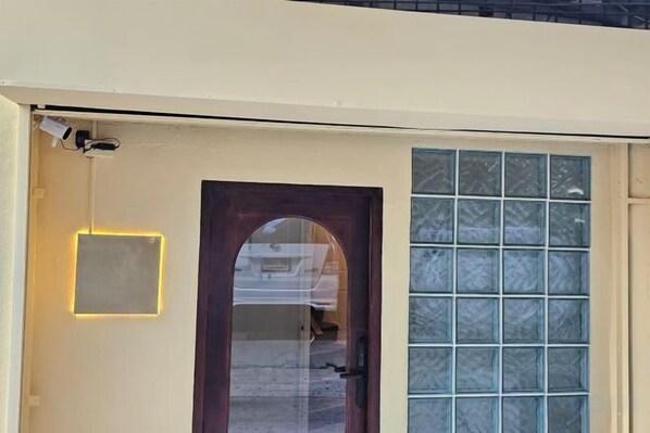 Eine Tür mit Fensterteil, einer kleinen beleuchteten Beschilderung und einer Überwachungskamera.