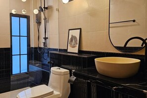 A bathroom with a large bowl sink, a toilet, a shower, and a framed picture on the wall. - Yaowarat Stay (Bangkok)