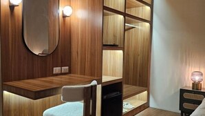 A modern bedroom with a wooden vanity, a mirror, a chair, a bedside table with a lamp, and a wardrobe with multiple compartments. - Yaowarat Stay (Bangkok)