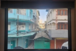 A narrow street view through a window with buildings on either side, including a green garage and a white vehicle in the foreground. - Yaowarat Stay (Bangkok)