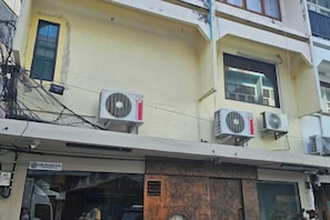 Un edificio de varios pisos con unidades de aire acondicionado en la fachada, un escaparate visible y un ventanal con vista a la calle.