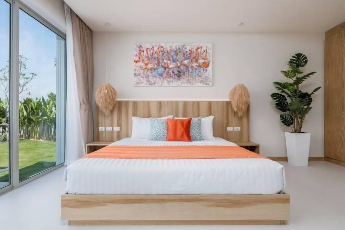 Camera da letto moderna con un letto grande, vista sul verde esterno, un'opera d'arte appesa al muro e una pianta in vaso.
