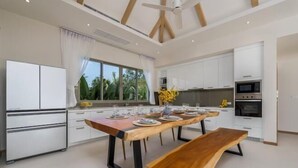 A modern kitchen with white cabinets, a wooden dining table, and a built-in oven. - Two Flamingo Villa 2 (Phuket)