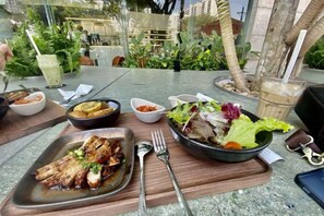 A dining table with various dishes, including a bowl of salad, a plate of grilled meat, and a drink. - Lena Condotel (Ho Chi Minh City)