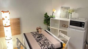 Une cuisine compacte équipée d’un four à micro-ondes, d’un petit réfrigérateur, d’une table à manger recouverte d’une nappe à motifs floraux et d’un grand lampadaire.