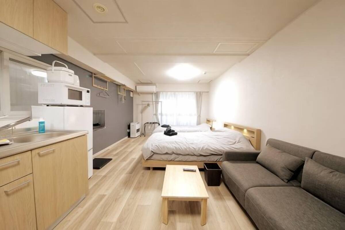 A compact hotel room with a kitchenette, a bed, a sofa, and a small table.