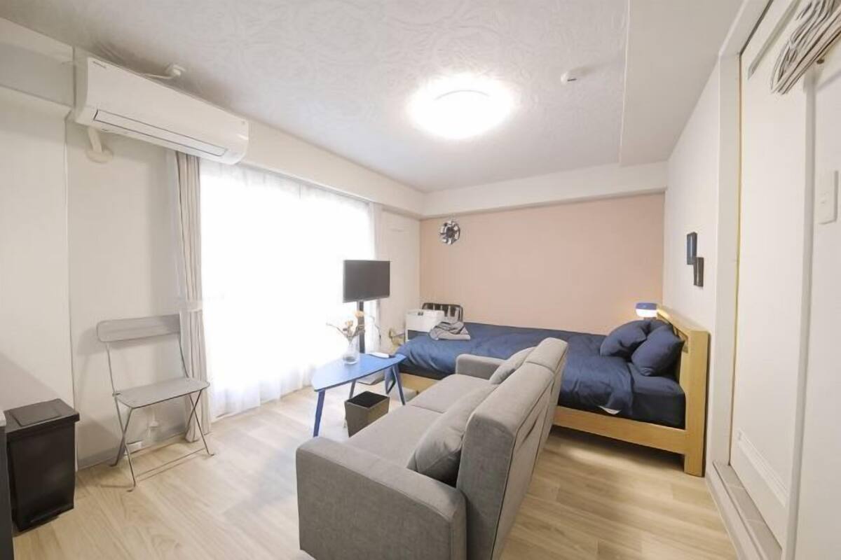 A room with a bed, a sofa, a desk with a lamp, and a window.