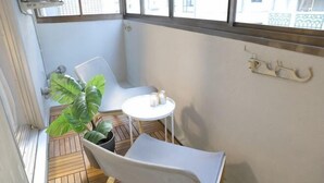 A balcony with a white chair, a small table with two salt and pepper shakers, and a potted plant. - Mansion Cattleya. (Sapporo)