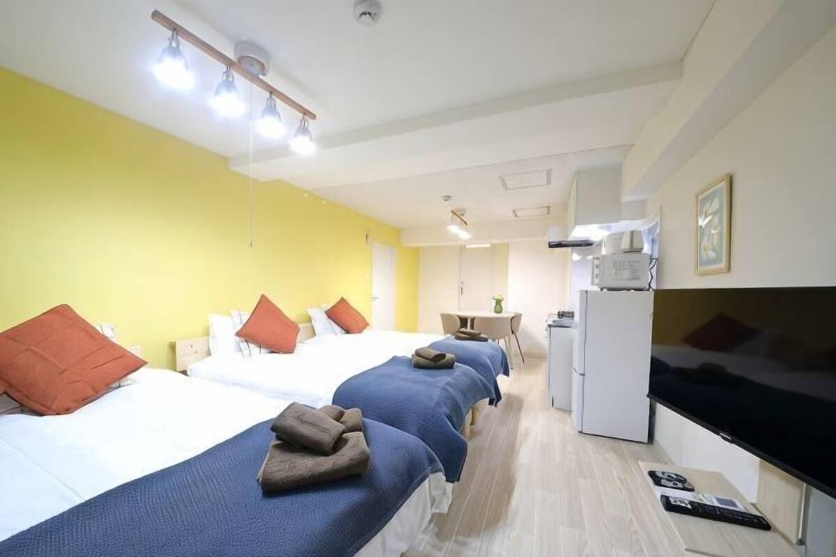 A hotel room with three beds, a kitchenette, a desk, and a mirror.