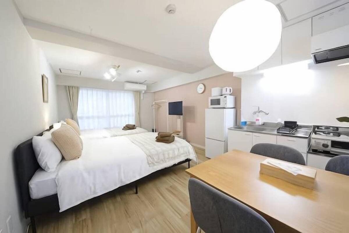 A hotel room with a bed, a desk, a chair, a microwave, a refrigerator, and a window with curtains.