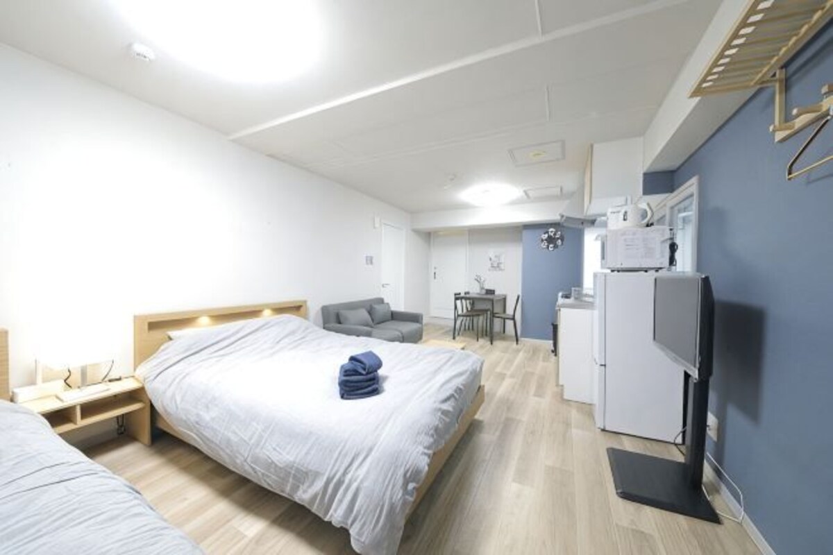 A hotel room with two beds, a desk, a chair, a refrigerator, and a television.