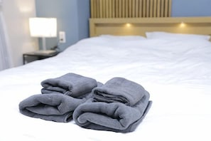 A neatly made bed with folded towels and a bedside lamp.
