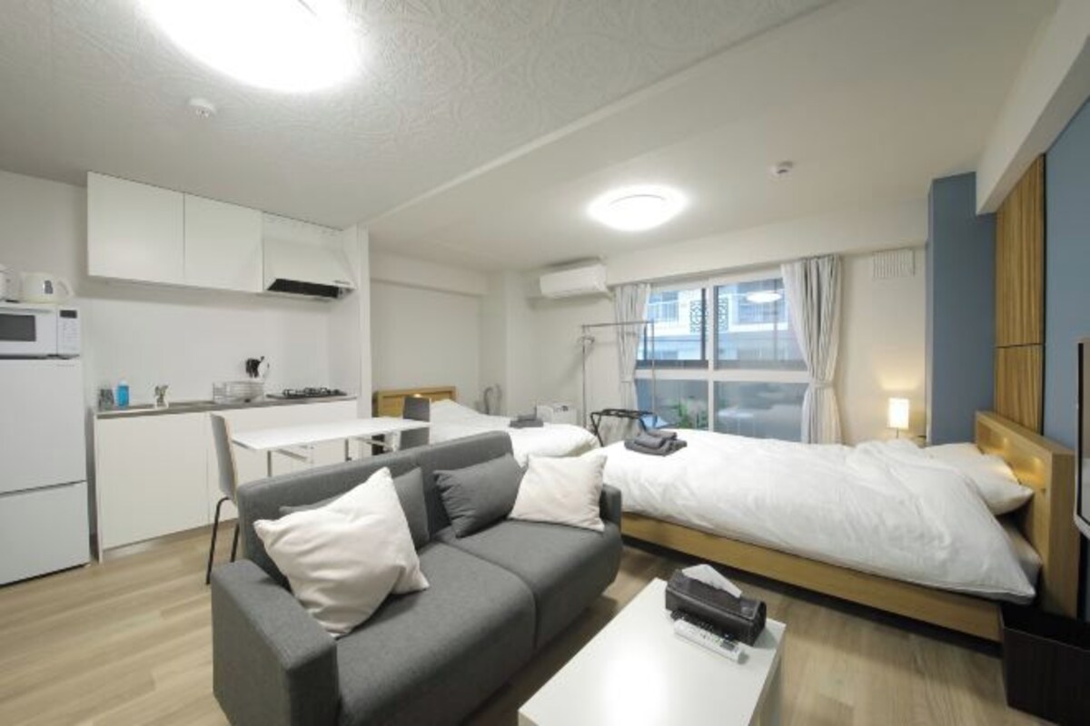 A compact hotel room with a kitchenette, a sofa, a bed, and a TV.
