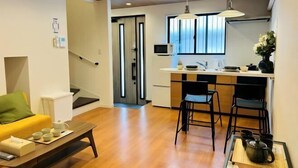 A modern living room with a sofa, coffee table, and a kitchen area with a dining table and chairs. - ASOBO OSAKA Kuromon 3rd (Osaka)