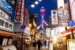 A busy street with illuminated signs and a prominent tower in the background. - ASOBO OSAKA Kuromon 3rd (Osaka)
