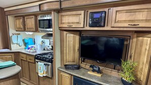 A compact kitchen with wooden cabinets, a microwave, a stove, and a flat-screen TV. - Cozy RV in quaint Nicholson. Close to UGA. (Nicholson)