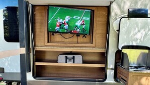 A recreational vehicle with a television mounted on the back wall, a foldable table, and a cushioned seating area. - Cozy RV in quaint Nicholson. Close to UGA. (Nicholson)