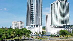 Two high-rise buildings with a view of a body of water and a road with cars. - Bay Win La.mer Butik (Kota Kinabalu)